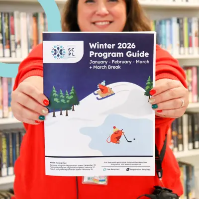 Woman in bright red sweater holding out the library's latest printed program guide.