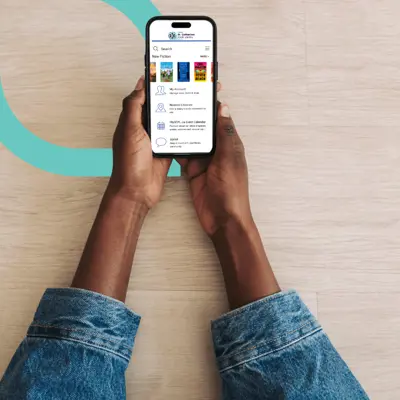Hands holding a phone displaying the library's app home screen.
